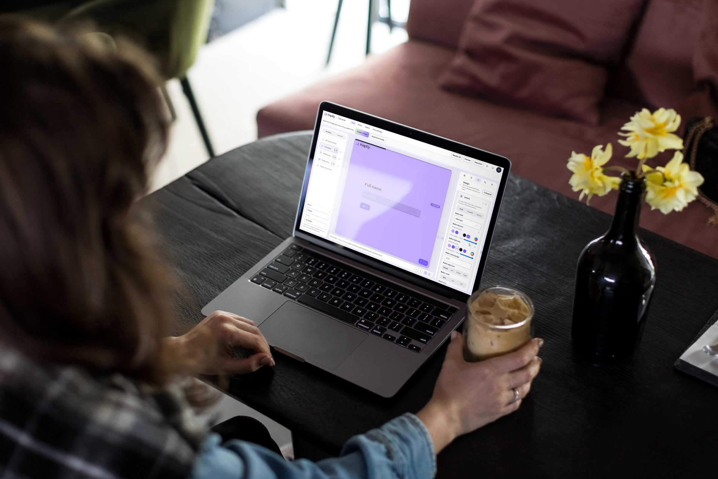 Žena za stolom u kafiću pravi Kaptly formu na laptopu, sa panelom za dizajn otvorenim pored platna